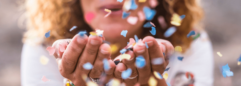 A picture of colourful confetti being blown in the direction of the camera by a woman.