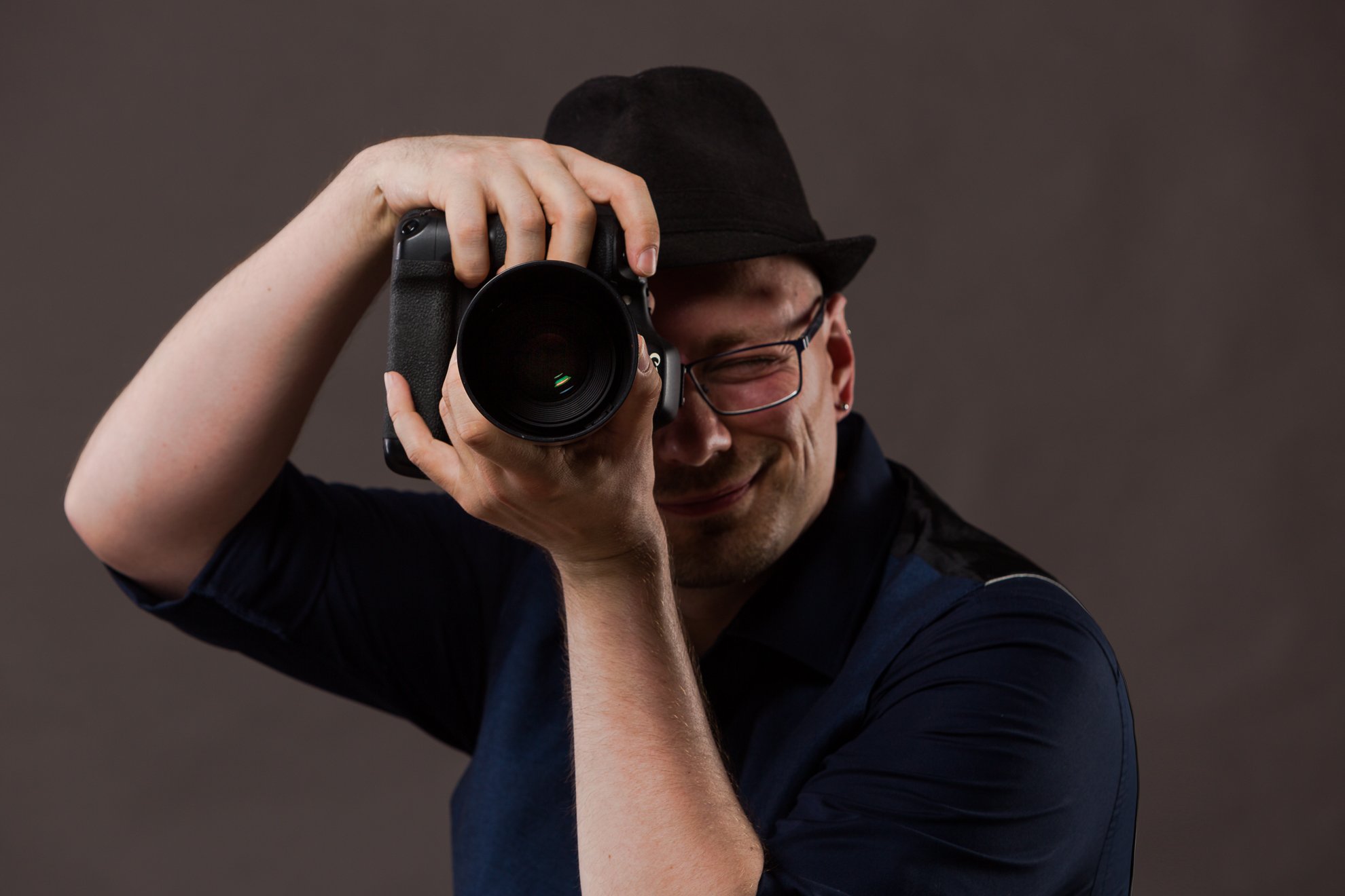 Mann mit Brille und Hut fotografiert die Person, die gerade das Foto macht.