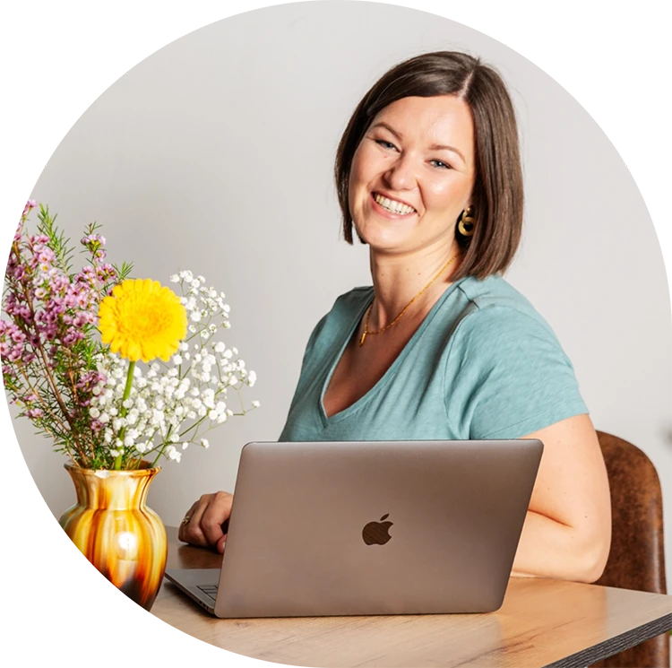 Birgit Spalt-Zoidl lächelt in die Kamera, vor ihr ist ein Laptop und daneben steht ein Blumenstrauß.